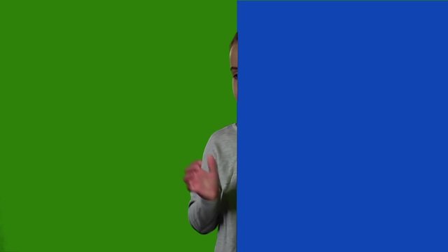 Child looks out from behind the blue board and laughs. Green screen. Slow motion
