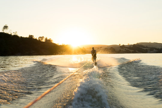 A water skier takes a run at sunset on a empty glassy lake