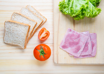 slices of bread with jam and ham, tamoto, lettuce on table with kitchen