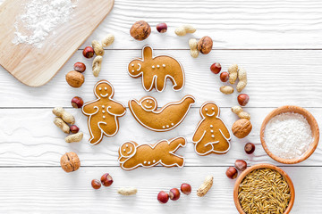 Healthy food for sportsman. Cookies in shape of yoga asanas near nuts on white wooden background...