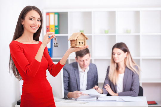 Cheerful realtor giving house key to happy property owners, young man taking keys to rented or purchased home, making deal with real estate agent, couple just signed contract and bought own flat