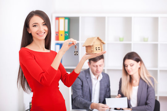 Cheerful realtor giving house key to happy property owners, young man taking keys to rented or purchased home, making deal with real estate agent, couple just signed contract and bought own flat