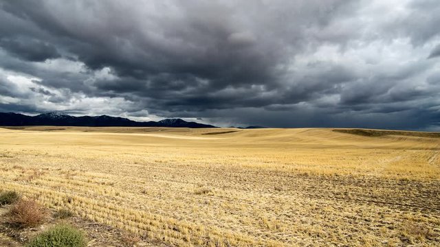 Time lapse of dramatic clouds over rolling fields or cut grain in Idaho farmland.