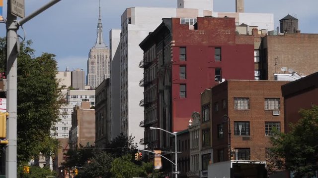 A daytime summer exterior establishing shot of typical apartment buildings and stores in midtown Manhattan. The Empire State Building is seen in the distance.  	