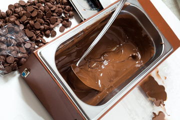 A close-up of a large mettalic container with liquid hot chocolate, next to it are small pieces of solid Belgian chocolate