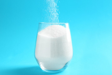 Glass with granulated sugar on color background