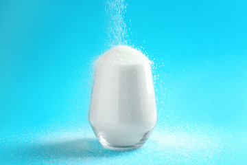 Glass with granulated sugar on color background