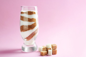 Glass with different types of sugar on color background