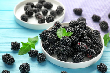 Plate with delicious ripe blackberries on color wooden background
