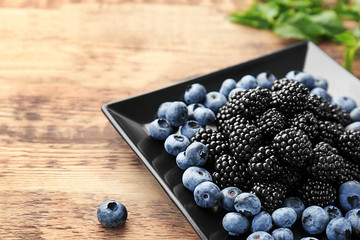 Plate with delicious blackberries and blueberries on wooden background