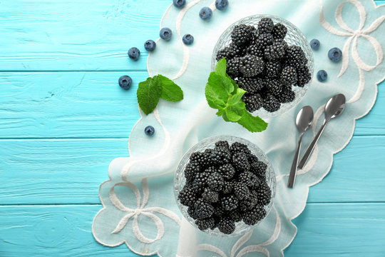 Dessert bowls with delicious ripe blackberries on color wooden background
