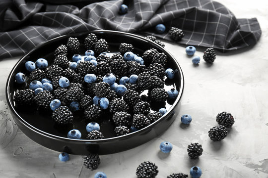 Plate with delicious ripe blackberries and blueberries on grey background