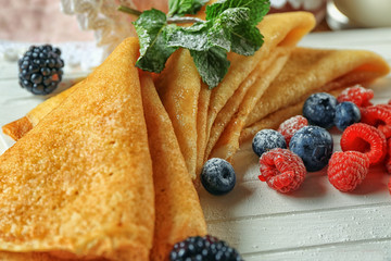 Tasty thin pancakes with berries on board, closeup