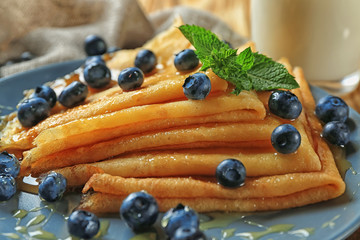 Tasty thin pancakes with blueberries on plate, closeup