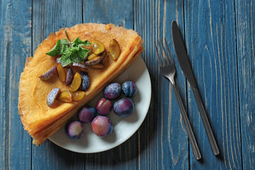 Plate with tasty thin pancakes and plums on table