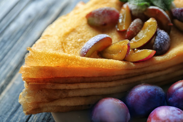 Tasty thin pancakes with plums on plate, closeup