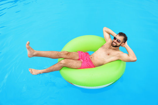 Handsome young man with inflatable ring relaxing in blue swimming pool