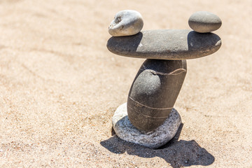 Fototapeta na wymiar Balancing gray pebbles on top of a stone on a sandy background. Stones pile background. Scales balance.