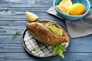 Plate with baked sweet potato and guacamole on wooden table