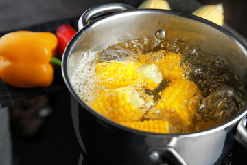 Saucepan with corn cobs on stove