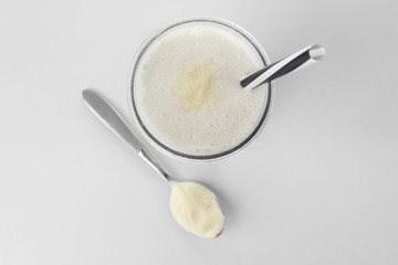 Fototapeta na wymiar Glass with protein shake and powder in spoon on white background