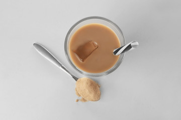 Glass with protein shake and powder in spoon on white background