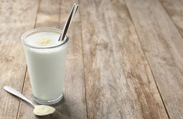 Glass with protein shake and powder in spoon on wooden table