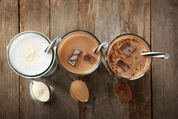 Glasses with different protein shakes and powders in spoons on wooden table