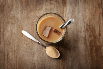 Glass with protein shake and powder in spoon on wooden table