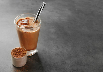 Glass with protein shake and powder in scoop on table