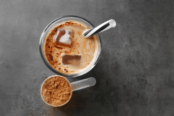 Glass with protein shake and powder in scoop on table