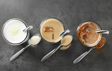 Glasses with different protein shakes and powders in spoons on table