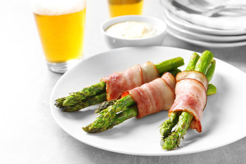 Plate with bacon wrapped asparagus on light background