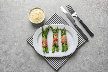 Plate with bacon wrapped asparagus on light background