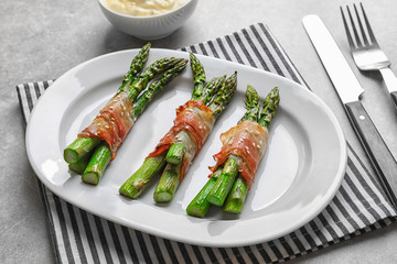 Plate with bacon wrapped asparagus on light background