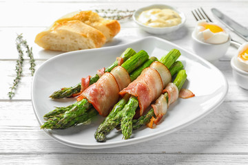 Plate with bacon wrapped asparagus on light background