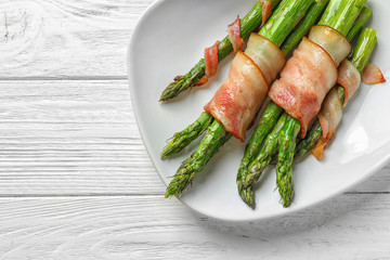 Plate with bacon wrapped asparagus on light background