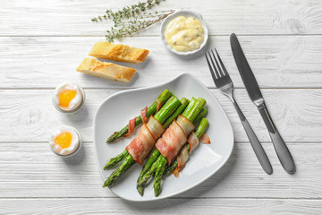 Plate with bacon wrapped asparagus on light background