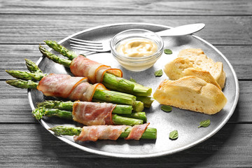 Plate with bacon wrapped asparagus on light background