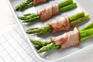 Plate with bacon wrapped asparagus on light background