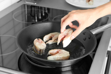Woman frying fish steaks on pan in kitchen
