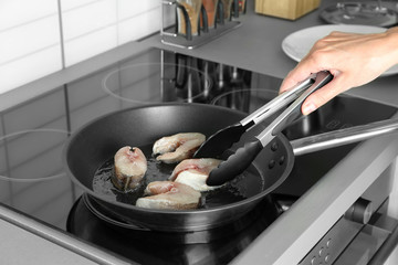 Woman frying fish steaks on pan in kitchen