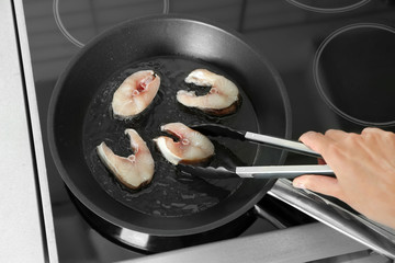Woman frying fish steaks on pan in kitchen
