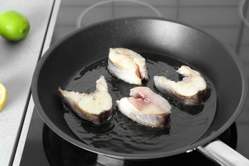 Frying pan with raw fish steaks on stove in kitchen