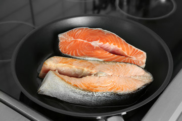 Frying pan with salmon steaks on stove in kitchen