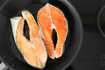 Frying pan with salmon steaks on stove in kitchen