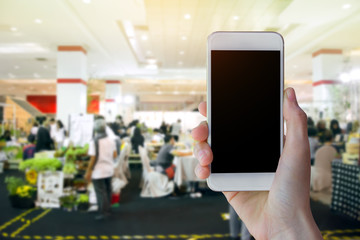 Hand holding mobile phone with Blurred people in food center and shopping mall backgroundl.