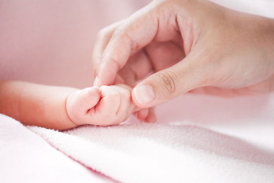 Mother hand holding asian newborn baby girl hand while she sleeping with love