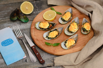 Mussels baked with spinach and Parmesan cheese with lemon and mint on a wooden desk