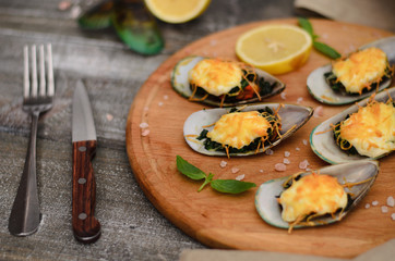 Mussels baked with spinach and Parmesan cheese with lemon and mint on a wooden desk